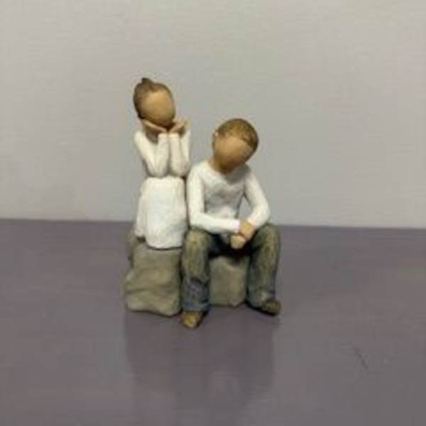 Two small figurines of seated people on a plain surface