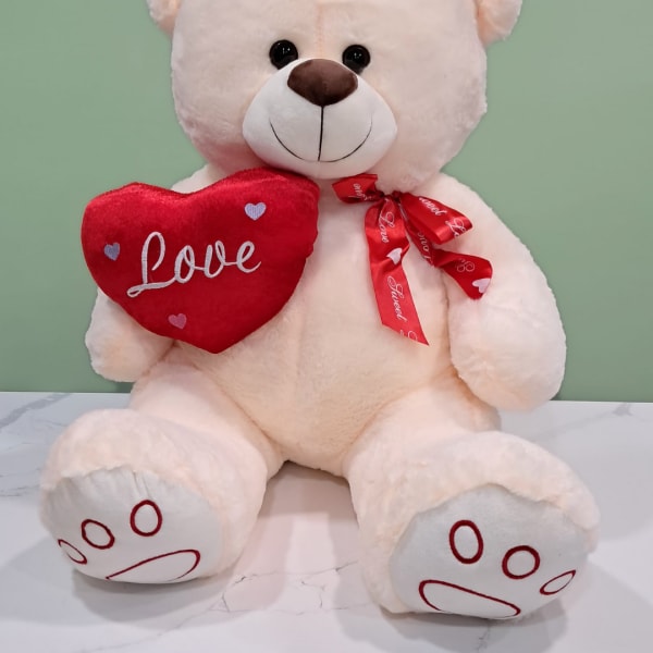 Plush teddy bear holding a red heart pillow