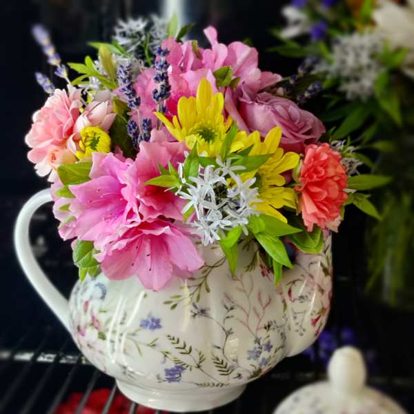 Pink and yellow flowers arranged in a floral teapot vase