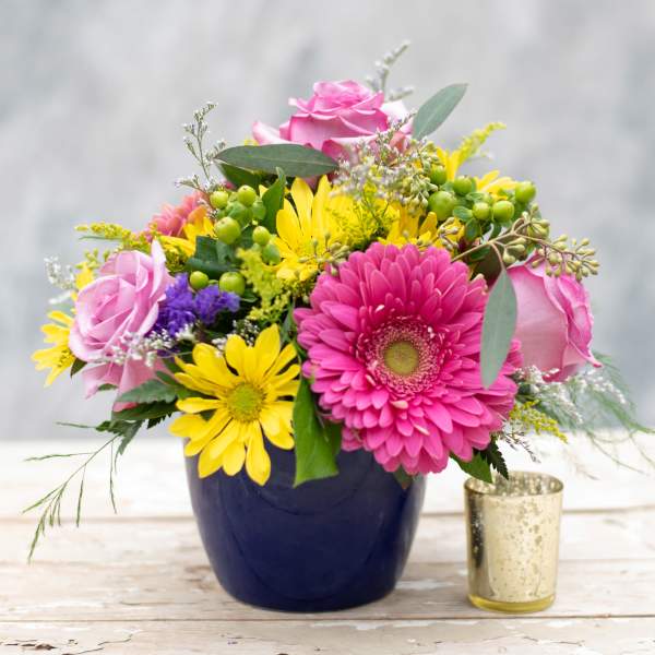 Pink roses and yellow daisies in a dark vase with a small gold candle holder
