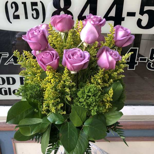 Pink roses arranged in a clear glass vase with yellow filler flowers