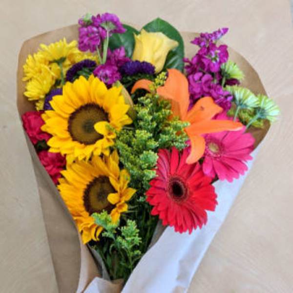Bouquet of sunflowers, gerbera daisies, and mixed blooms wrapped in paper