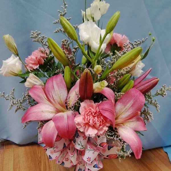 Pink lilies and carnations arranged with white blooms in a ribboned bouquet