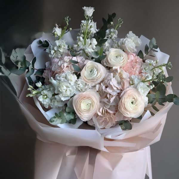 Pastel bouquet of white and blush flowers wrapped in pale pink paper