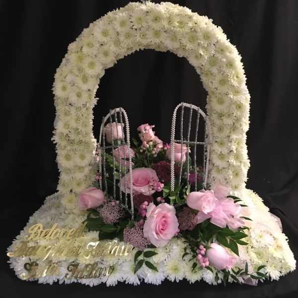 White floral funeral arch with pink roses and a cross topper