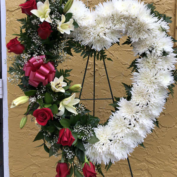 Tall heart-shaped white wreath with red roses and white lilies on a metal easel stand