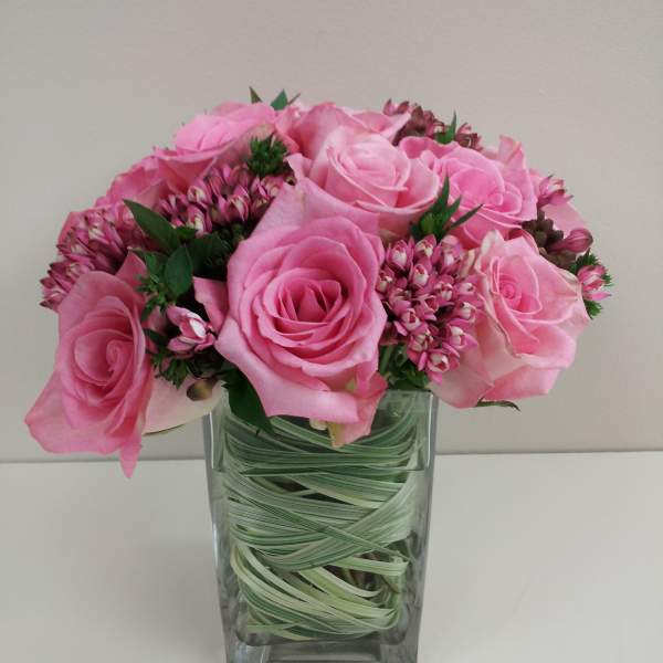 Pink roses and small pink filler flowers in a clear square vase