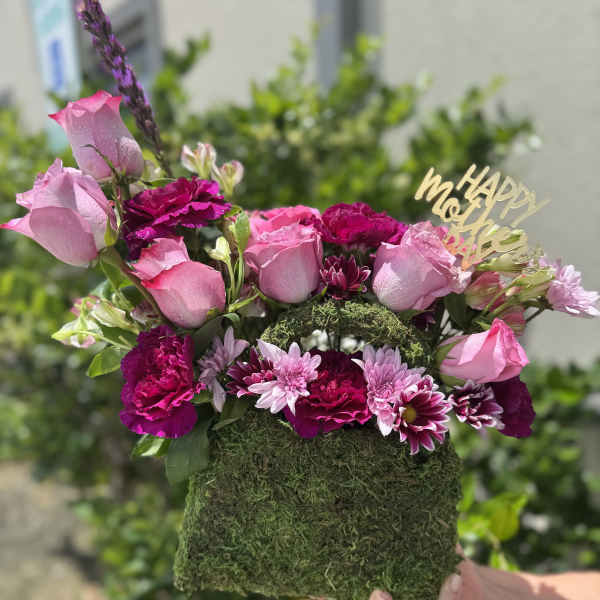 Pink roses and magenta flowers in a moss-covered box with a gold "Happy Mother's Day" topper