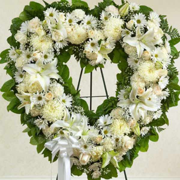 Heart-shaped white floral wreath on a stand with a white ribbon