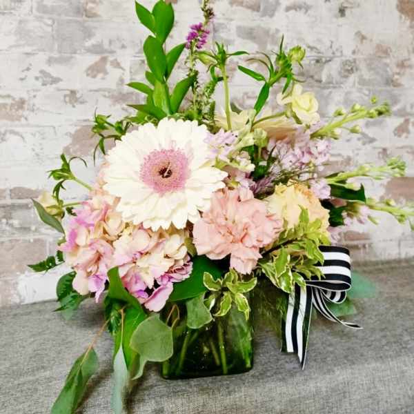 Pastel flower arrangement in a green glass vase with a striped ribbon