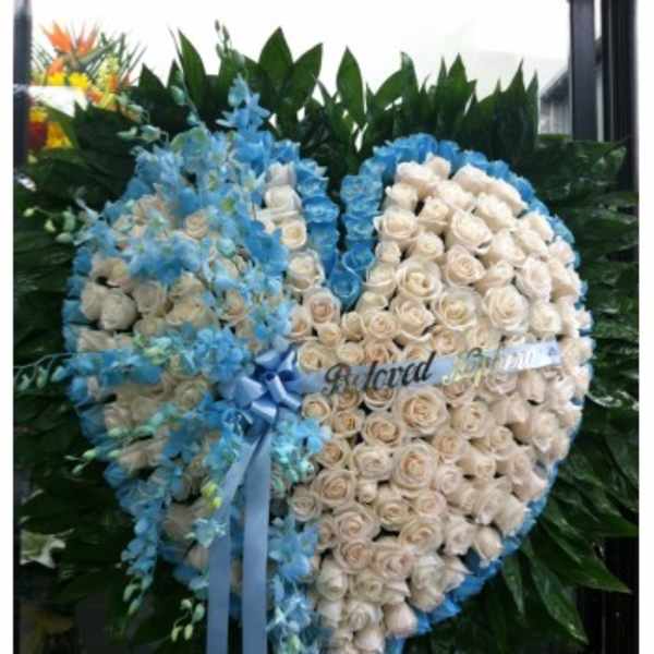 Heart-shaped floral wreath of white roses and blue flowers with a ribbon