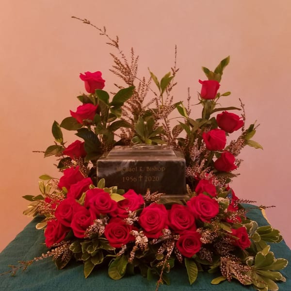 Red rose cremation wreath surrounding a dark urn on a teal-covered table