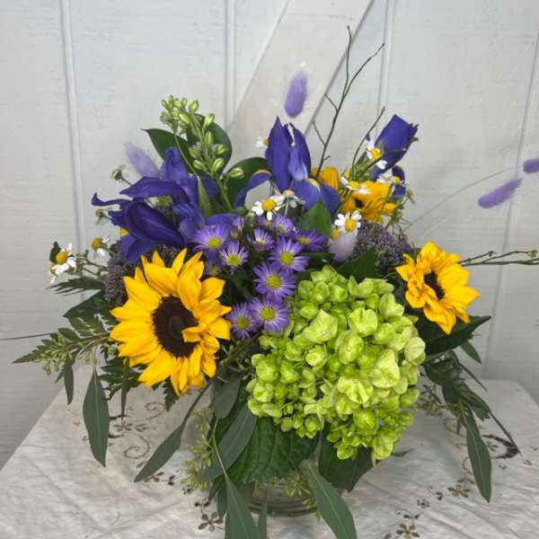 Bouquet with sunflowers, purple blooms, and green hydrangea in a glass vase