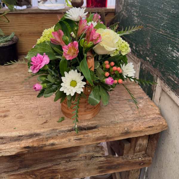 Mixed flower arrangement in a small wicker basket with pink, white, and cream blooms
