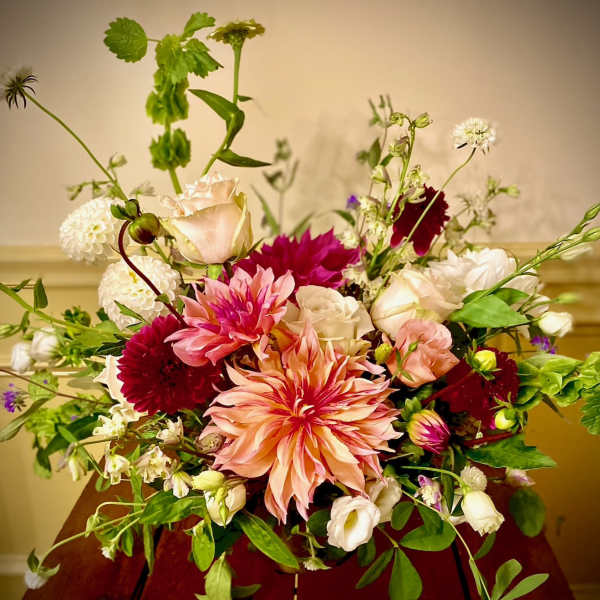 Airy arrangement of peach dahlias with pink and white roses in a low vase on a wooden table