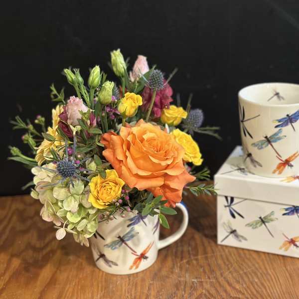 Orange and yellow flower arrangement in a dragonfly mug beside a matching mug and box