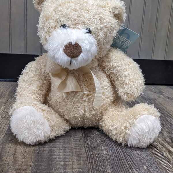 Cream teddy bear with a ribbon bow sitting on a wooden floor