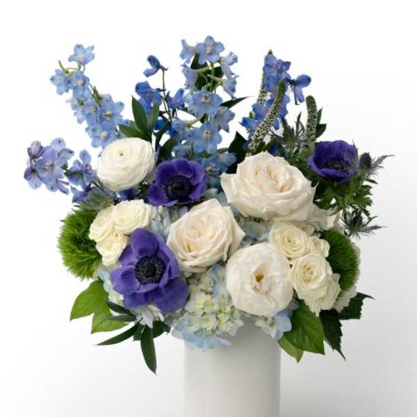 White and blue flower arrangement with roses and anemones in a tall white cylinder vase