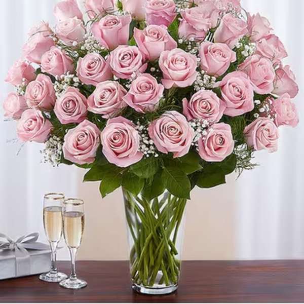 Pink roses arranged in a clear glass vase with a gift box and champagne flutes nearby