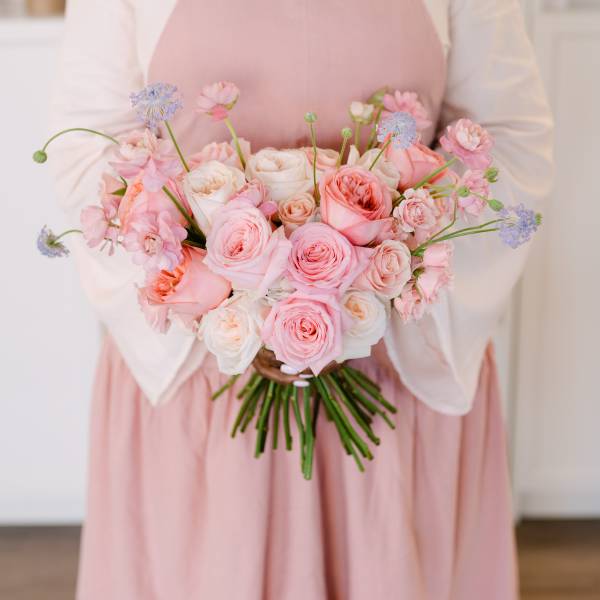 Person holding a bouquet of pink and white roses with small blue flowers