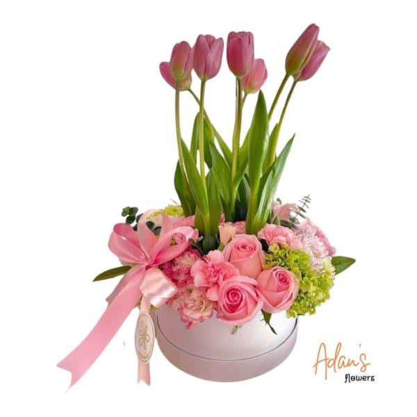 Pink tulips and roses arranged in a round box with a ribbon