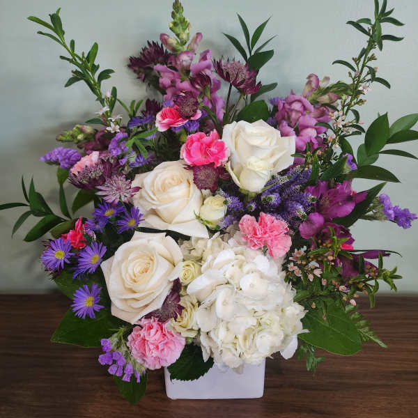 Mixed bouquet of white roses, hydrangea, and pink-purple flowers in a white vase