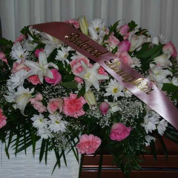 Pink and white funeral spray with a satin ribbon on a casket