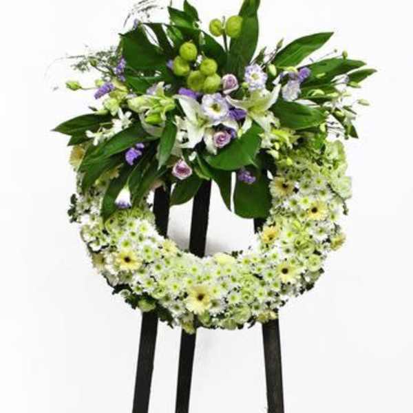Standing floral wreath with white and green flowers on a black easel