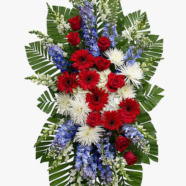 Tall standing spray with red roses, red gerberas, white mums, and blue delphinium on palm leaves