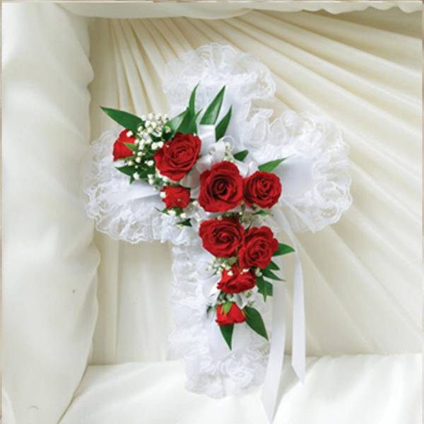 White lace cross with red roses and white filler flowers on a cream fabric background