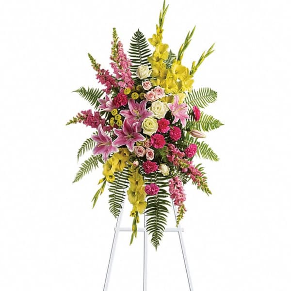 Tall standing spray of pink lilies, roses, and yellow flowers on a white easel