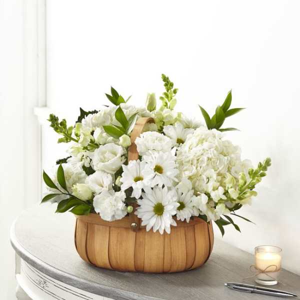 White flowers arranged in a wooden basket with a candle beside it