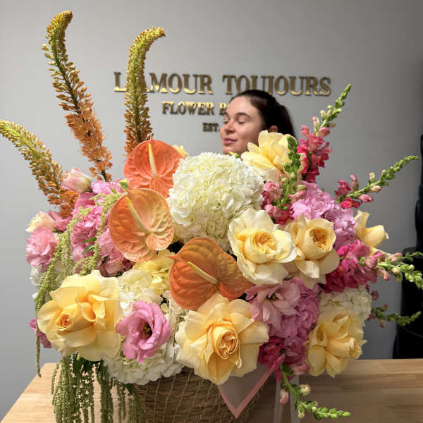 Large pastel flower arrangement in a wicker basket with roses and anthuriums