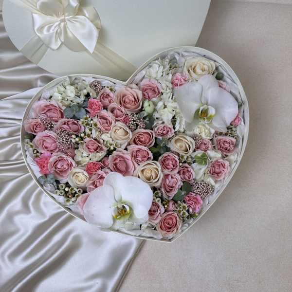 Heart-shaped box filled with pink and ivory roses and white orchids on a satin background