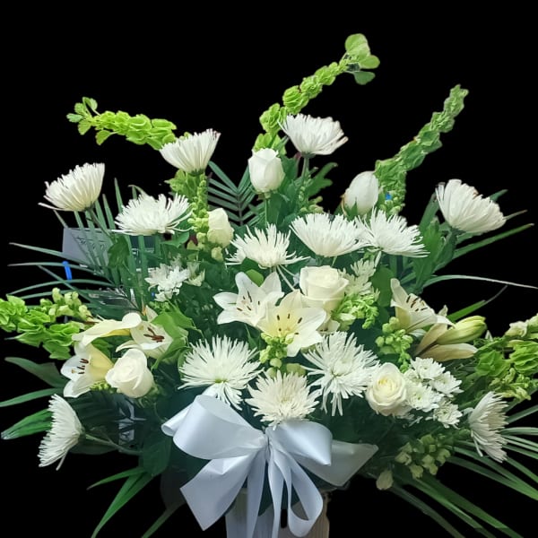 White floral arrangement with lilies, roses, and a white ribbon
