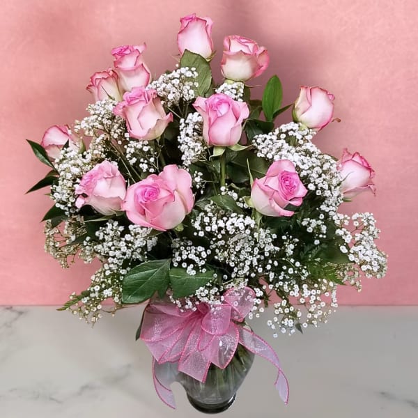 Pink roses with baby's breath in a glass vase tied with a pink ribbon