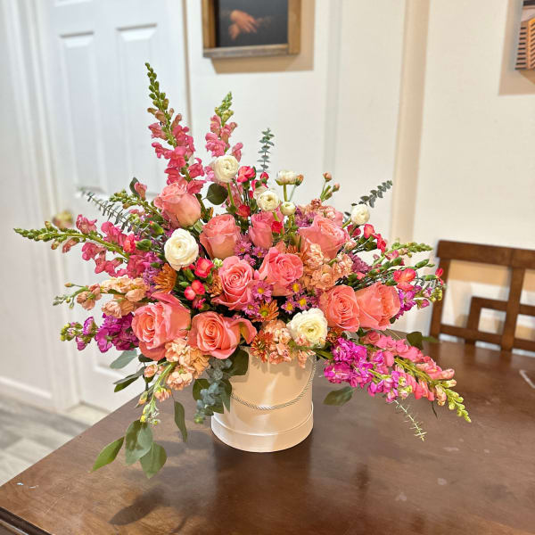 Pink and peach floral arrangement in a white hatbox-style container