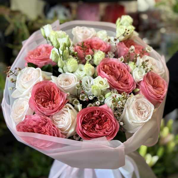 Pink and white rose bouquet wrapped in pale pink paper with a white ribbon