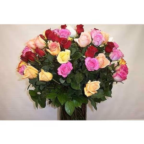 Tall arrangement of mixed red, pink, yellow, and peach roses in a clear glass vase