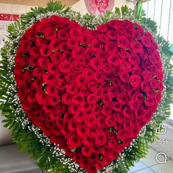 Heart-shaped arrangement of red roses with white filler flowers and greenery