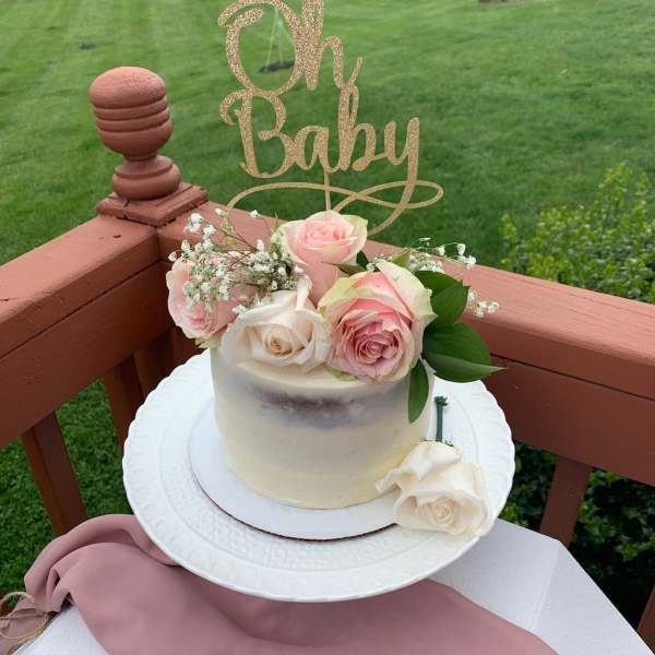 Small cake topped with pink and white roses and a glittery "Oh Baby" sign
