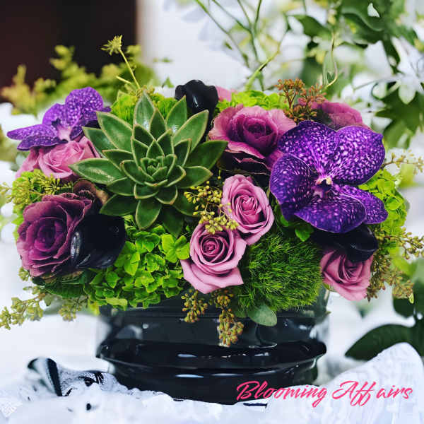 Purple orchids and pink roses arranged with a central succulent in a black vase