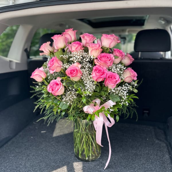 Pink roses arranged in a clear glass vase with baby's breath and a pink ribbon