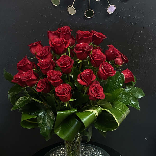 Red roses arranged in a clear vase with glossy leaves