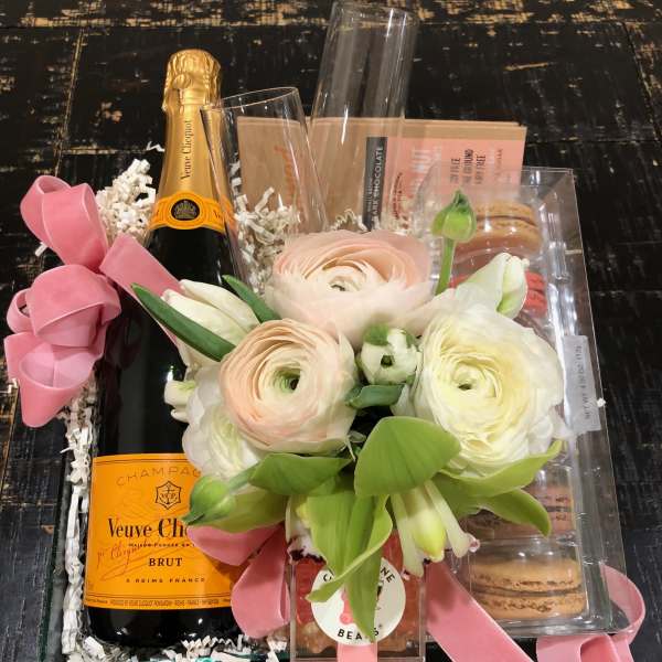 Gift basket with flowers, champagne, macarons, and candy in a clear tray