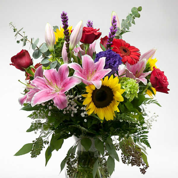 Mixed bouquet of lilies, roses, and sunflowers in a glass vase
