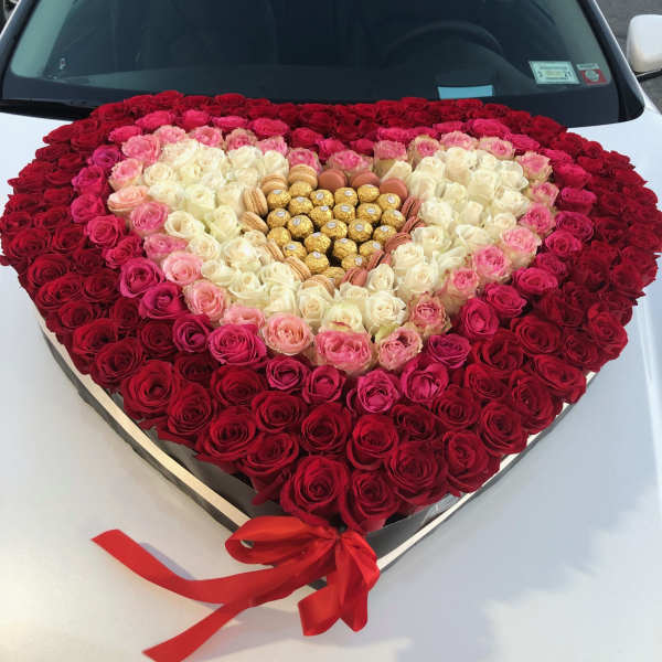 Heart-shaped rose arrangement with chocolates and a red ribbon
