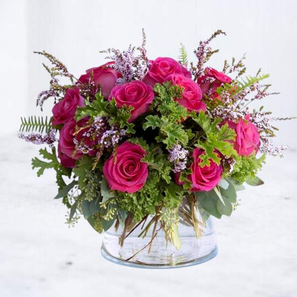 Pink roses arranged in a clear glass vase with greenery and small filler flowers