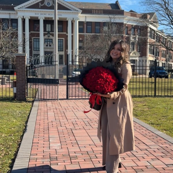 Woman holding a large bouquet of red roses in front of a school building