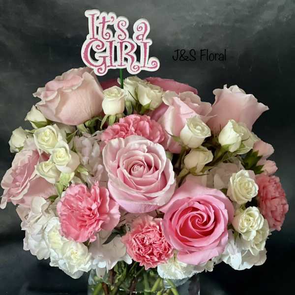 Pink and white rose bouquet in a clear vase with an "It's a Girl" topper.